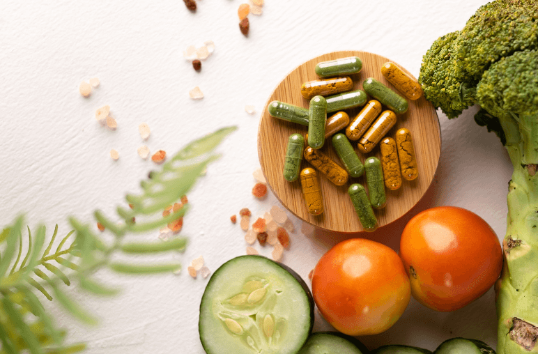Various dietary supplements in capsules on a wooden plate surrounded by fresh vegetables like cucumbers, tomatoes, and broccoli, emphasizing the connection between nutrition and autophagy.